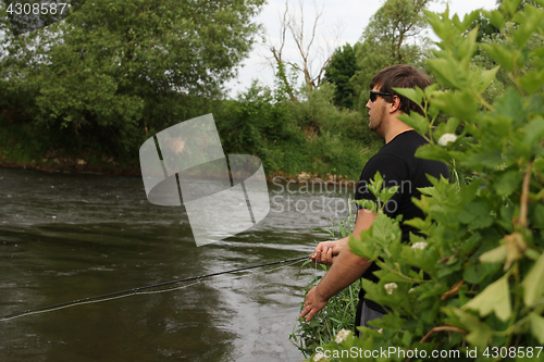 Image of Young man with fishing rod fishing at a river