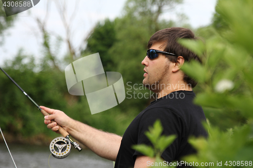 Image of Young man with fishing rod fishing at a river 