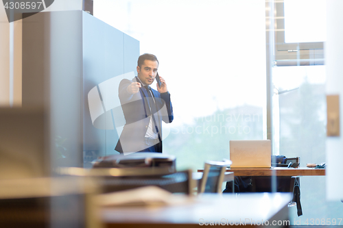 Image of Businessman talking on a mobile phone in corporate office, pointing to camera.