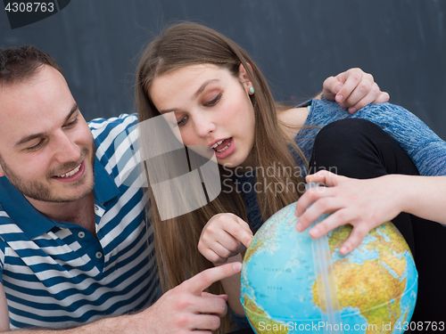 Image of couple in casual clothing investigating globe