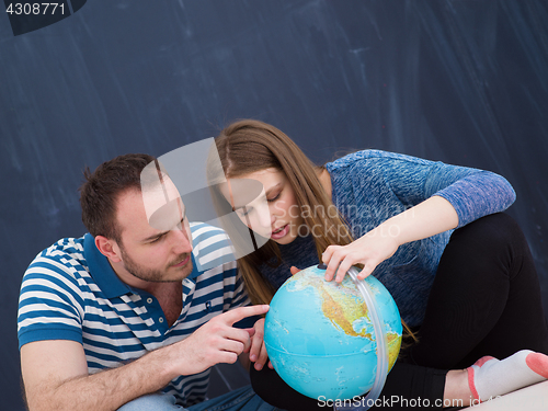 Image of couple in casual clothing investigating globe