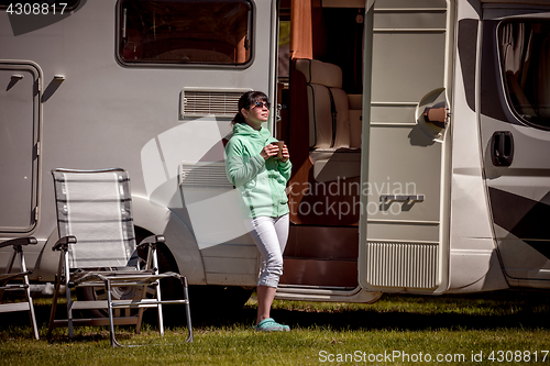 Image of Woman is standing with a mug of coffee near the camper.