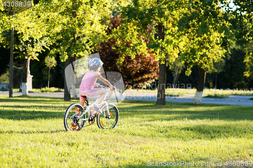 Image of happy child girl riding bicycle in summer sunset