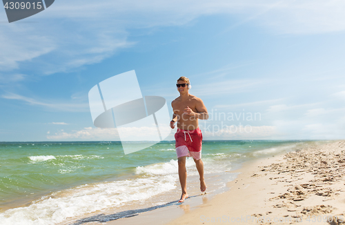 Image of happy man with headphones running along beach