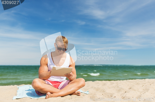 Image of happy smiling young man with tablet pc on beach