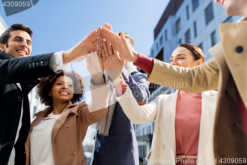 Image of group of happy people making high five in city