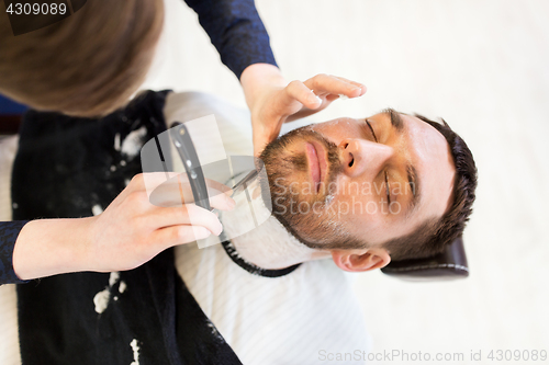 Image of man and barber with straight razor shaving beard