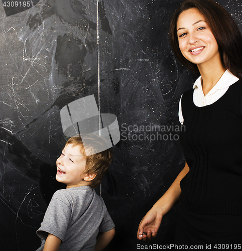 Image of little cute boy with young teacher in classroom studying at blac