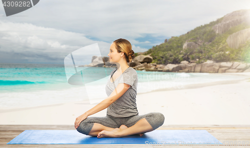 Image of woman doing yoga in twist pose on beach