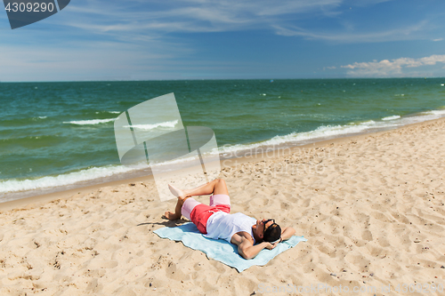 Image of happy smiling young man sunbathing on beach towel