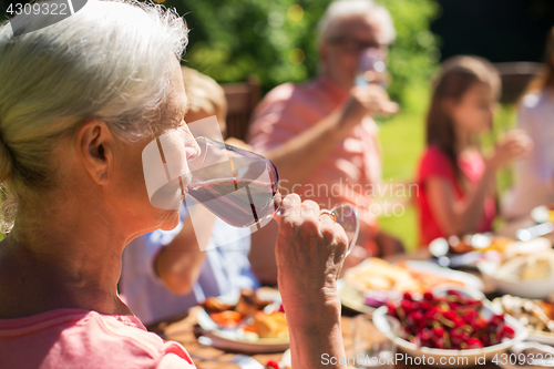 Image of senior woman drinking wine at family dinner