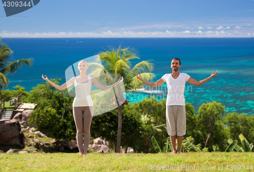 Image of happy couple making yoga exercises on beach