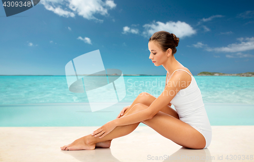 Image of beautiful woman touching her smooth legs on beach