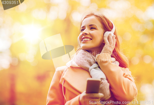 Image of woman with smartphone and earphones in autumn park