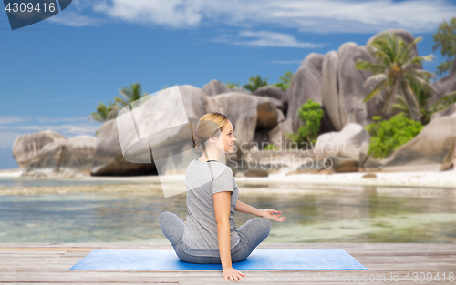 Image of woman doing yoga in twist pose on beach