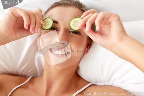 Image of beautiful woman applying cucumbers to eyes at home