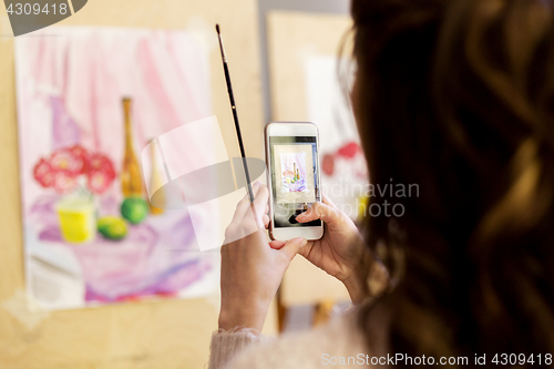 Image of woman with painting on smartphone at art school