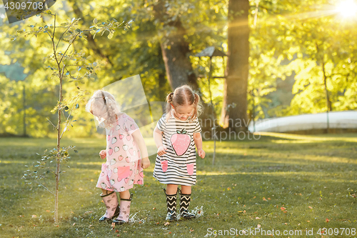 Image of The cute little blond girls in rubber boots playing with water splashes on the field in summer