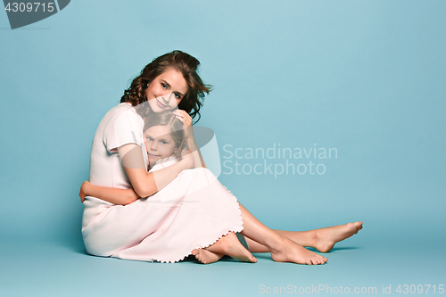 Image of Pregnant mother with teen daughter. Family studio portrait over blue background