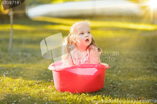 Image of The cute little blond girl playing with water splashes on the field in summer