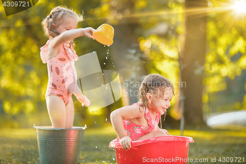 Image of The cute little blond girls playing with water splashes on the field in summer