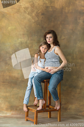 Image of Pregnant mother with teen daughter. Family studio portrait over blue background