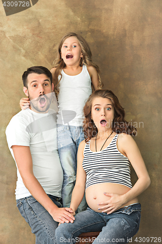 Image of Pregnant mother with teen daughter and husband. Family studio portrait over brown background