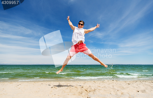 Image of smiling young man jumping on summer beach