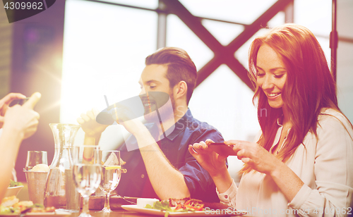 Image of happy friends taking picture of food at restaurant