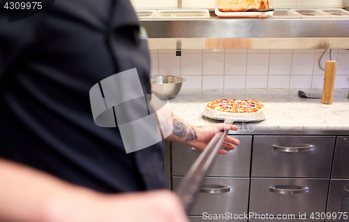 Image of cook or baker with pizza on peel at pizzeria