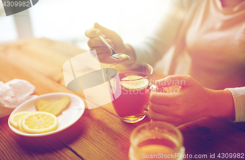 Image of close up of woman adding honey to tea with lemon