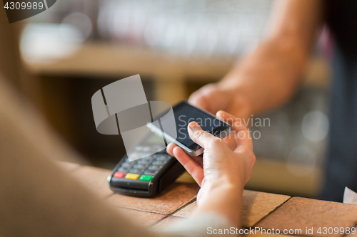 Image of hands with payment terminal and smartphone at bar