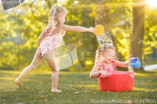 Image of The cute little blond girls playing with water splashes on the field in summer