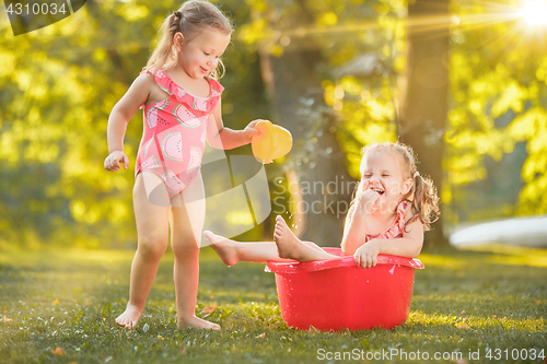 Image of The cute little blond girls playing with water splashes on the field in summer