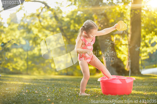 Image of The cute little blond girl playing with water splashes on the field in summer