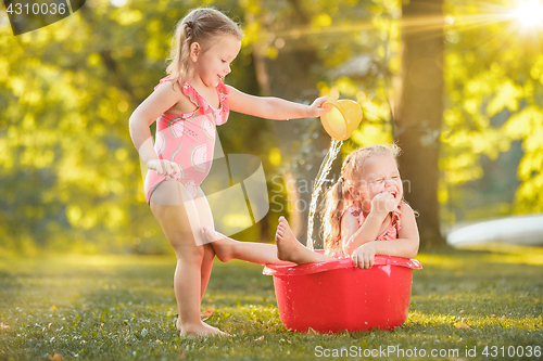 Image of The cute little blond girls playing with water splashes on the field in summer