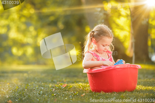 Image of The cute little blond girl playing with water splashes on the field in summer