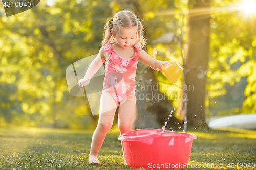 Image of The cute little blond girl playing with water splashes on the field in summer