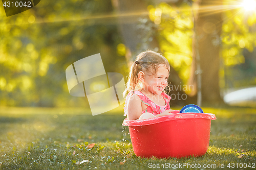 Image of The cute little blond girl playing with water splashes on the field in summer