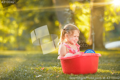 Image of The cute little blond girl playing with water splashes on the field in summer