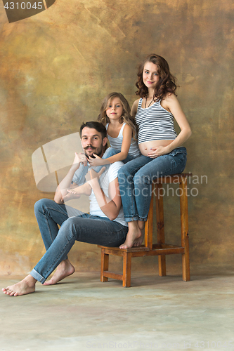 Image of Pregnant mother with teen daughter and husband. Family studio portrait over brown background