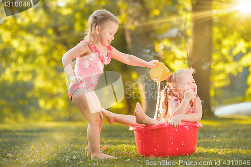 Image of The cute little blond girls playing with water splashes on the field in summer