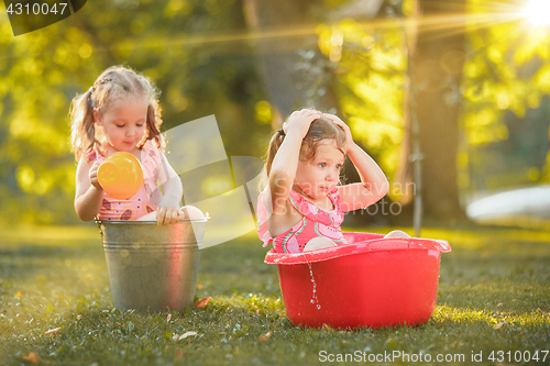 Image of The cute little blond girls playing with water splashes on the field in summer