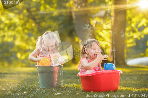 Image of The cute little blond girls playing with water splashes on the field in summer