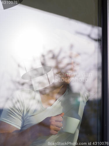 Image of young man drinking morning coffee by the window