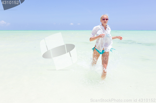 Image of Young active woman having fun running and splashing in shellow sea water.