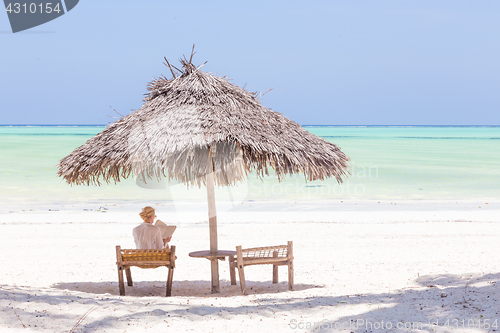 Image of Women relaxing on dack chair under wooden umbrella on tropical beach.