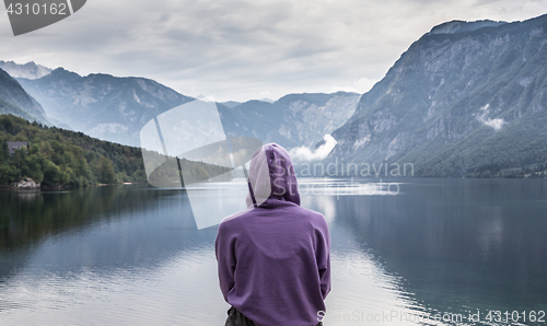 Image of Woman wearing purple hoodie watching tranquil overcast morning scene at lake Bohinj, Alps mountains, Slovenia.