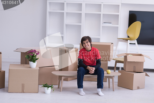 Image of boy sitting on the table with cardboard boxes around him