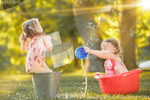 Image of The cute little blond girls playing with water splashes on the field in summer